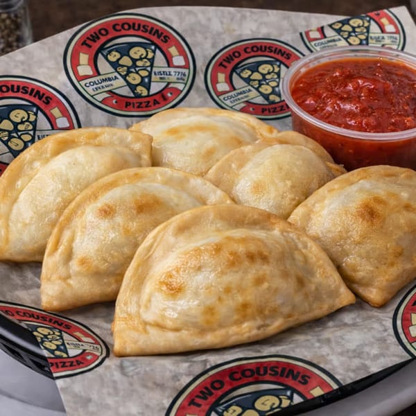 Golden-brown Two Cousins Pizza pierogies with a side of marinara sauce, served in a basket.