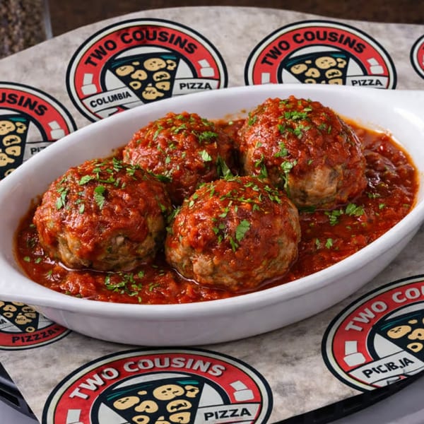 Four large meatballs covered in red sauce and parsley in a white dish, on a Two Cousins Pizza branded paper.