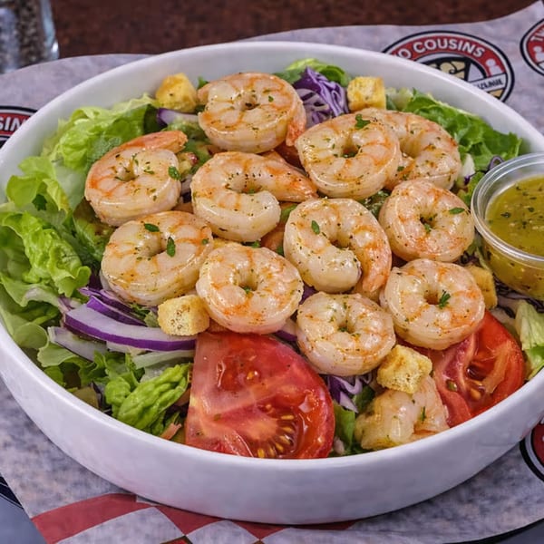 Shrimp salad with lettuce, red onion, tomatoes, croutons, and a side of dressing.